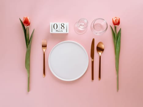 8 march table setting. Empty white plate, calendar with march eight date and red tulip on pink background. Aesthetic stylish dinner table setting for Women's day. Copy space. Flat lay