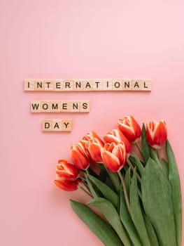 International women's day or eight march concept with copy space. International women's day text and bunch of red tulip on pink background. Top view or flat lay. Vertical