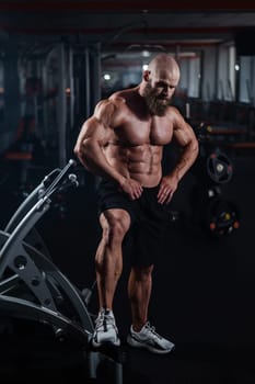 Muscular bald man posing in shorts. Bodybuilder showing off his shape in the gym