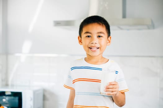 Portrait of smiling Asian little boy in kitchen holding milk. Cute son enjoys drink, radiating joy. Young child savoring calcium-rich liquid, feeling happy at home give me.