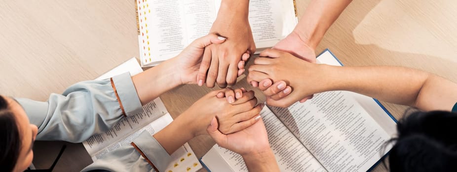 Cropped image of diversity people hand praying together at wooden church on bible book while hold hand together with believe. Concept of faith, god blessing concept. Top view. Burgeoning.