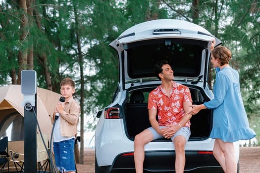 Outdoor adventure and family vacation camping in nature travel by eco friendly car for sustainable future. Lovely family recharge EV car with EV charging station in campsite. Perpetual