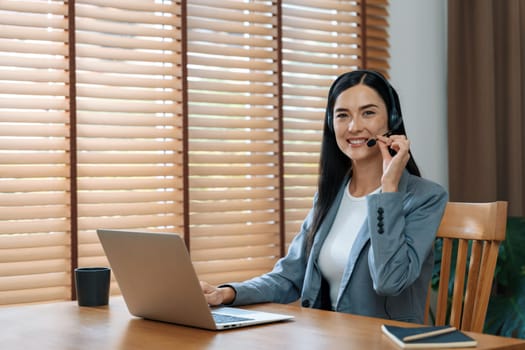 Female call center operator or customer service helpdesk staff working on workspace while talking on the headset to provide assistance for customer. Professional modern business service. Blithe