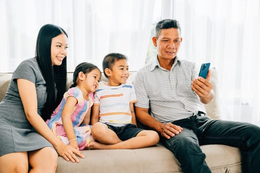 Parents and kids laugh watching a video on a smartphone seated together on a couch. This image reflects familial happiness bonding and shared moments of technology enjoyment.