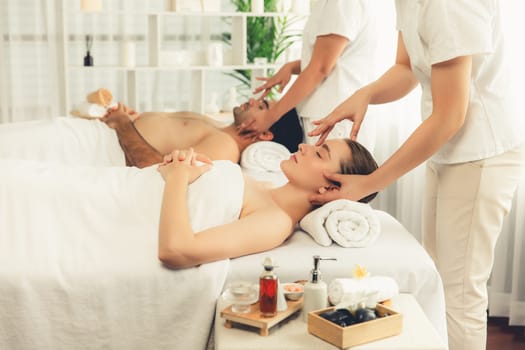 Caucasian couple enjoying relaxing anti-stress head massage and pampering facial beauty skin recreation leisure in dayspa modern light ambient at luxury resort or hotel spa salon. Quiescent