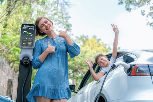 Family road trip vacation with electric vehicle, mother and son recharge EV car with green and clean energy. Nature and travel with eco-friendly car for sustainable environment. Perpetual