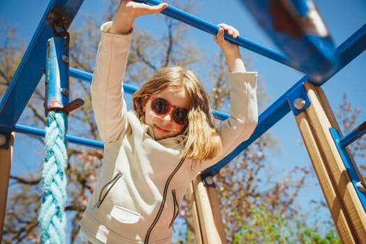 Cute little girl climbing on a playground equipment on the blu sky background