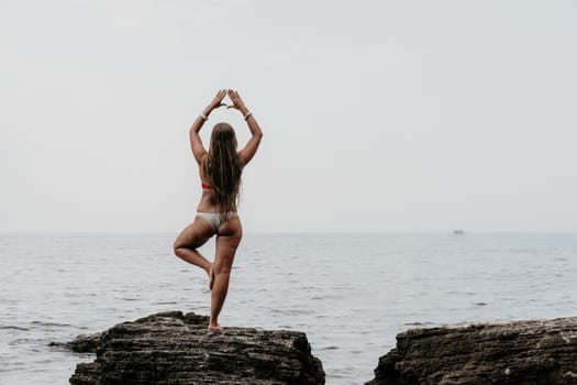 Woman meditating in yoga pose silhouette at the ocean, beach and rock mountains. Motivation and inspirational fit and exercising. Healthy lifestyle outdoors in nature, fitness concept.