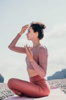 Young woman with long hair in white swimsuit and boho style braclets practicing outdoors on yoga mat by the sea on a sunset. Women's yoga fitness routine. Healthy lifestyle, harmony and meditation