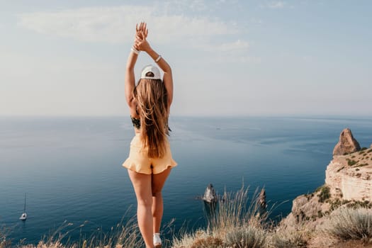 Woman travel sea. Happy tourist taking picture outdoors for memories. Woman traveler looks at the edge of the cliff on the sea bay of mountains, sharing travel adventure journey.