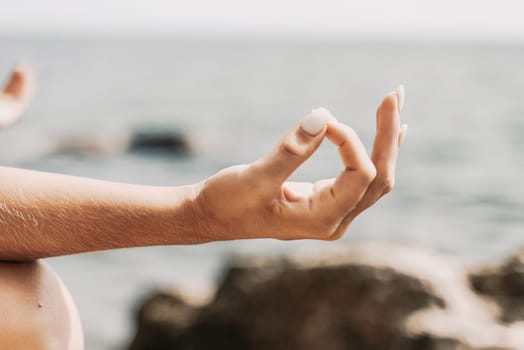 Yoga on the beach. A happy woman meditating in a yoga pose on the beach, surrounded by the ocean and rock mountains, promoting a healthy lifestyle outdoors in nature, and inspiring fitness concept