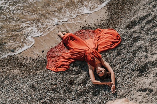 Woman red dress sea. Female dancer in a long red dress posing on a beach with rocks on sunny day.