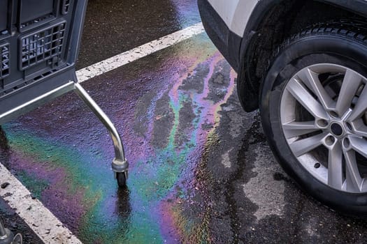 Gasoline and oil spill on wet asphalt in a parking lot near a hypermarket.