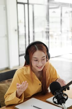 Cheerful woman hosting a live podcast, engaging with audience using professional microphone in studio.