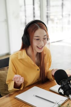 Cheerful woman hosting a live podcast, engaging with audience using professional microphone in studio.