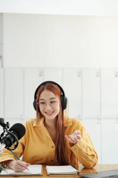 Cheerful woman hosting a live podcast, engaging with audience using professional microphone in studio.