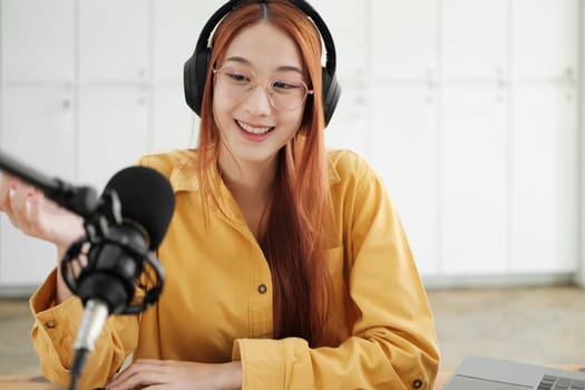 Cheerful woman hosting a live podcast, engaging with audience using professional microphone in studio.