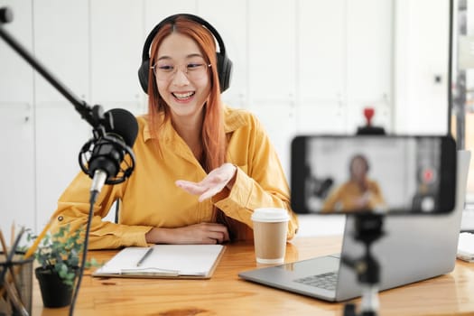 Cheerful woman hosting a live podcast, engaging with audience using professional microphone in studio.