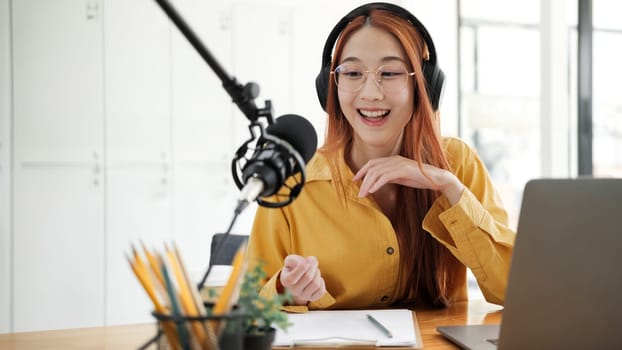 Cheerful woman hosting a live podcast, engaging with audience using professional microphone in studio.