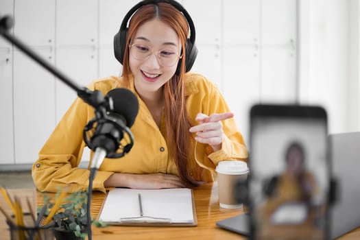 Cheerful woman hosting a live podcast, engaging with audience using professional microphone in studio.