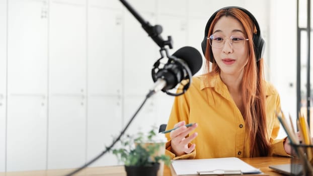 Cheerful woman hosting a live podcast, engaging with audience using professional microphone in studio.