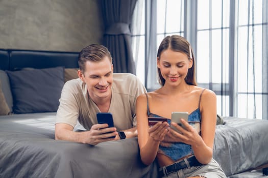 Young couple sit in the home bedroom using online payment app and digital wallet on smartphone to pay with credit card. E commerce shopping and modern purchasing via mobile internet. Unveiling