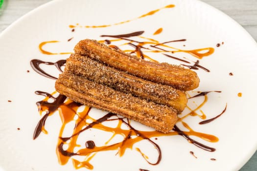 Hot churros with chocolate sauce on wooden table.