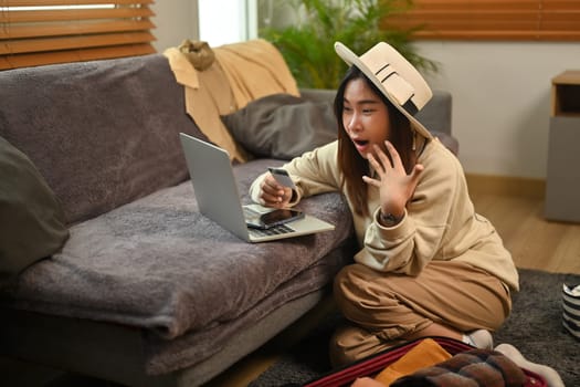 Excited young woman holding credit card and using laptop booking a trip online.