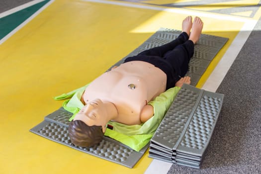 A mannequin for teaching artificial respiration of the whole body, lying on the yellow floor, spread out on a mat for a course of first aid and resuscitation