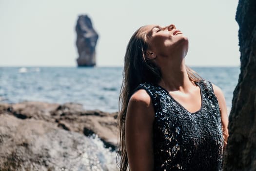 Woman travel sea. Young Happy woman in a long red dress posing on a beach near the sea on background of volcanic rocks, like in Iceland, sharing travel adventure journey