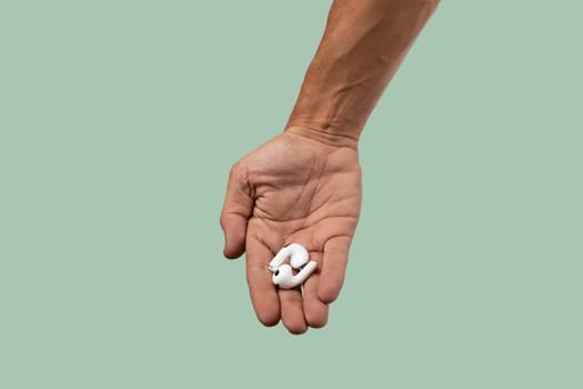 Male hand holding white earbuds on green background. High quality photo