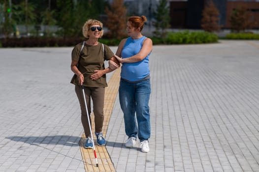 Caucasian pregnant woman leading blind elderly lady outdoors
