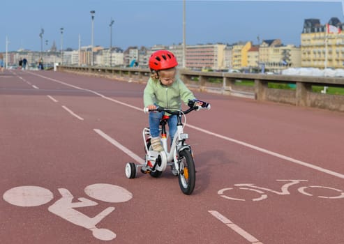 3 Years old Girl in helmet learns riding a four-wheeled bicycle