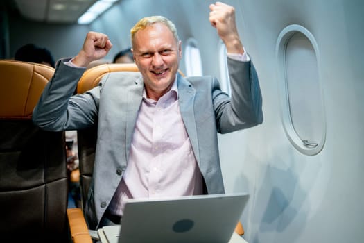 Senior business man express happiness action after see the successful of project or work from laptop during flight to working in the other city.