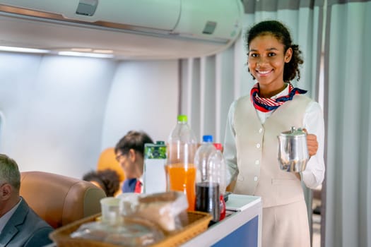 Portrait of air hostess hold teapot and look at camera with stand beside of trolley in the airplane during service of food and drinking to the passenger.