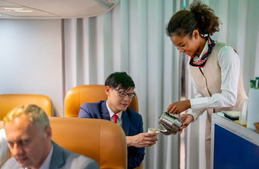 Air hostess hold teapot and give drinking to the passenger business man in the airplane.