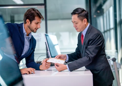 Airline staff give boarding pass to the passenger business man and explain about the detail at counter service in the airport.