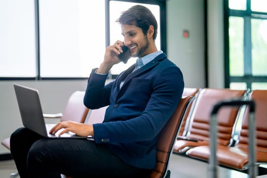 Smart business man sit at waiting area seat in airport and using laptop with mobile phone to working during wait to flight to the other city.