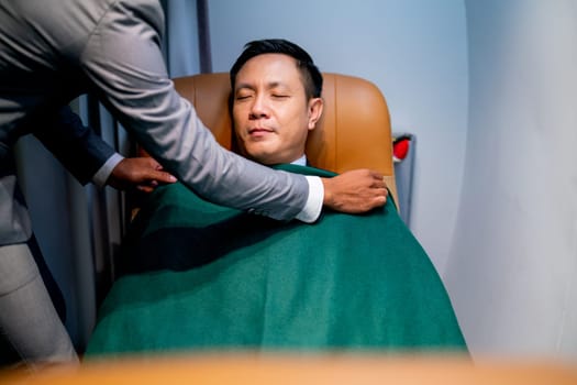 Airline staff help to cover the blanket to customer business man during flight for working.