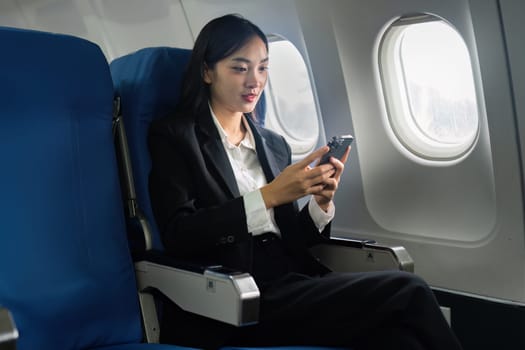 Beautiful Asian businesswoman using mobile phone in aeroplane. working, travel, business concept.