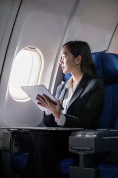Successful young asian business woman sits in airplane cabin plane and working from anywhere. Flying at first class.