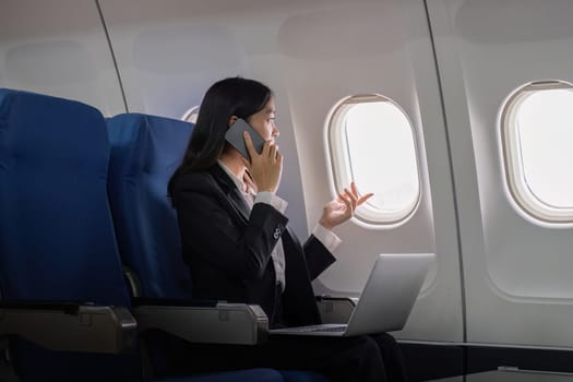 Successful young asian business woman sits in airplane cabin plane and working from anywhere. Flying at first class.