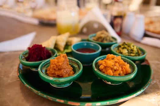 Food background with traditional Moroccan vegetarian salads served on small tagine dishes on a green ceramic plate. Moroccan culture and cuisine. Food and drink consumerism. Travel and tourism