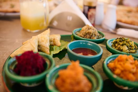 Food background with traditional Moroccan vegetarian salads served on small tagine dishes on a green ceramic plate. Moroccan culture and cuisine. Food and drink consumerism. Selective focus