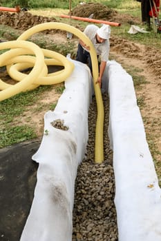 Groundwater drainage works in the field. A worker carries a yellow perforated drainage pipe.