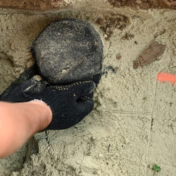 A plumber installs a reinforced orange sewer pipe during site maintenance. Hands of a plumber close-up near a sewer pipe covered with sand.