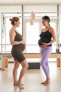 Two pregnant women communicate in a fitness club. Pilates for expectant mothers