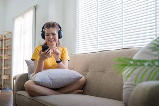 Young asian woman using mobile phone and earphones to listening to music or online chatting at home.