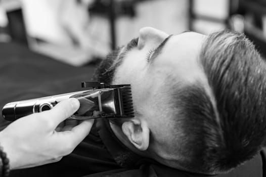 Cutting a gentleman beard in a barbershop with a clipper. Shortening the length of the beard from the sides by the master for the client.