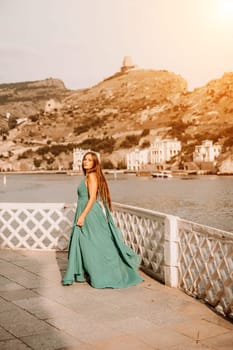 Woman sea trevel green dress. Side view a happy woman with long hair in a long mint dress posing on a beach with calm sea bokeh lights on sunny day. Girl on the nature on blue sky background